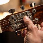 Pourquoi un instrument à cordes se dérègle et comment un luthier peut aider Gros plan sur une guitare acoustique en cours d’accordage, avec focus sur les mécaniques et les cordes dans un atelier de lutherie.
