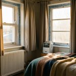 Réduire sa facture d’énergie dans une location mal isolée avant l’hiver Intérieur d’un appartement ancien préparé pour réduire sa consommation d’énergie avant l’hiver, avec rideaux épais, joints de fenêtre et couvertures en laine.